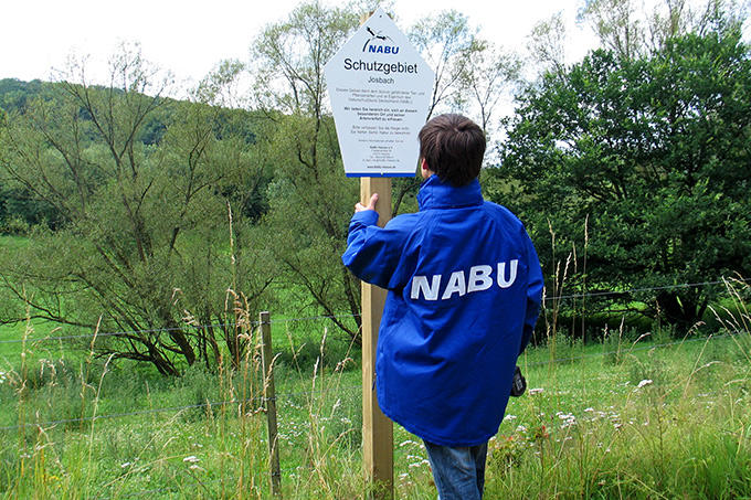 Das NABU-Schutzgebietsschild wird auf der Stiftungsfläche am Josbach montiert - Foto: Hartmut Mai