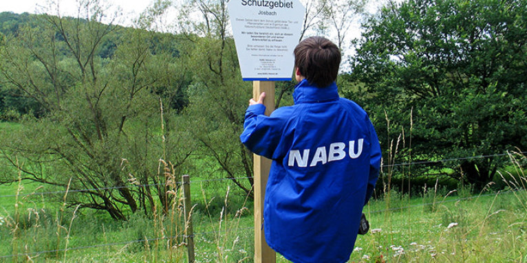 Das NABU-Schutzgebietsschild wird auf der Stiftungsfläche am Josbach montiert - Foto: Hartmut Mai